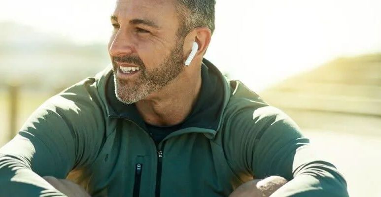 Uśmiechnięty mężczyzna w zielonej bluzie i słuchawkami w uszach