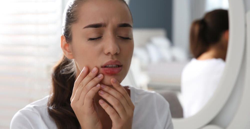 Młoda kobieta dotyka ust, na których znajdują się bolesne pęcherze