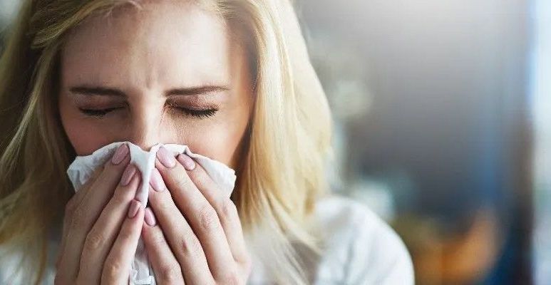 Młoda kobieta mrużąc oczy, wyciera nos chusteczką