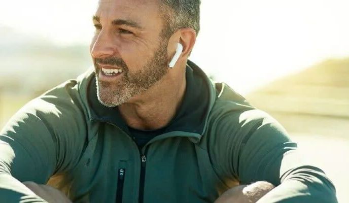 Uśmiechnięty mężczyzna w zielonej bluzie i słuchawkami w uszach