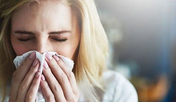 Młoda kobieta mrużąc oczy, wyciera nos chusteczką