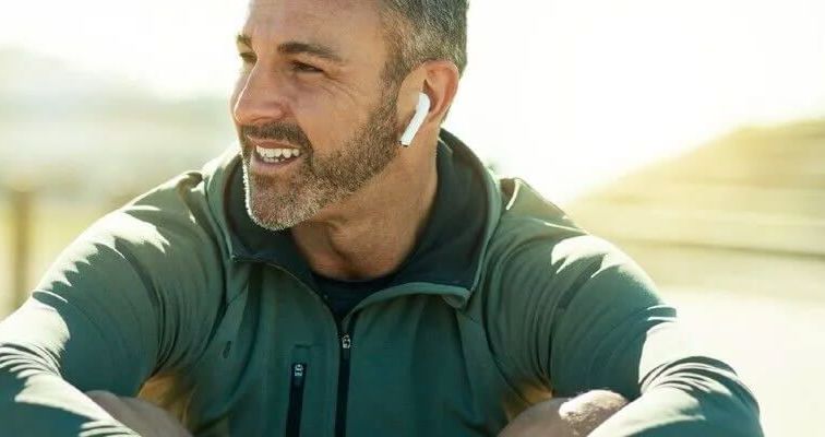 Uśmiechnięty mężczyzna w zielonej bluzie i słuchawkami w uszach