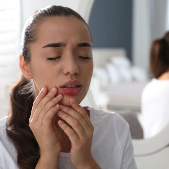 Młoda kobieta dotyka ust, na których znajdują się bolesne pęcherze