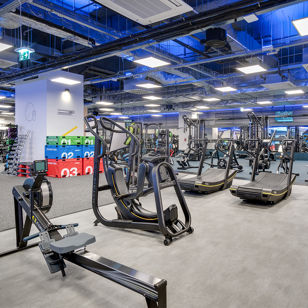 Siłownia z rowerem wioślarskim, eliptykiem oraz kolorowymi pojemnikami do ćwiczeń.