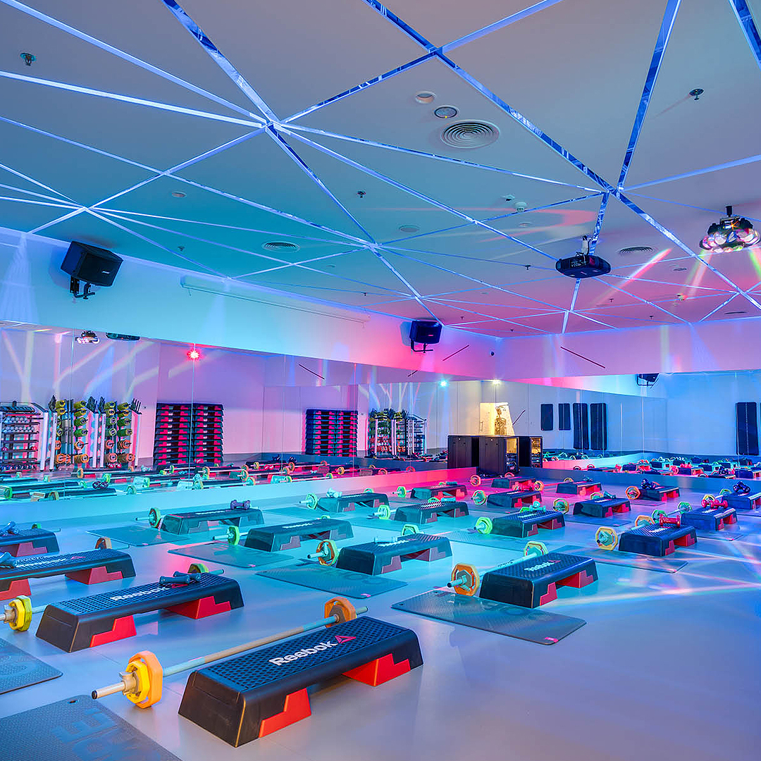 Sala fitness z stepami, hantlami i kolorowym oświetleniem.